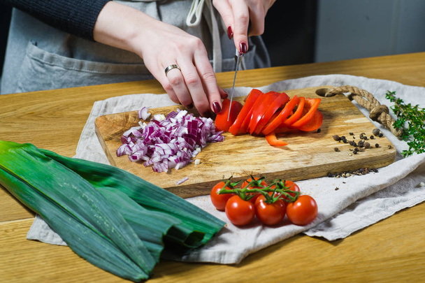 The chef cuts red bell peppers on a wooden chopping Board. Background kitchen, side view - 写真・画像