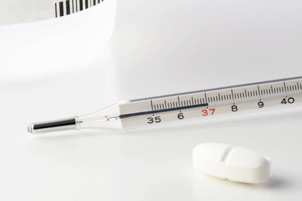 Медичний ртутний термометр і біла таблетка ізольовані на білому тлі. Вакцинація, грип, медицина, аптека, педіатрія та сучасні лабораторні концепції
. - Фото, зображення