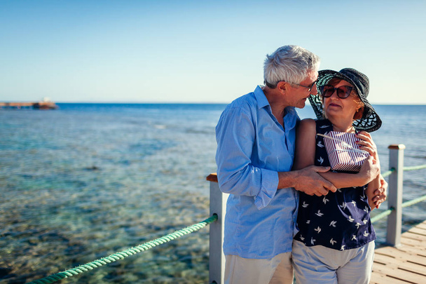 Ein älteres Ehepaar, das auf der Seebrücke unterwegs ist und Geschenke für den Valentinstag überreicht. glückliche Menschen genießen Urlaub. - Foto, Bild