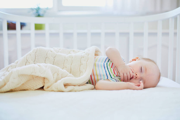 Adorable baby girl sleeping in co-sleeper crib attached to parents' bed. Little child having a day nap in cot. Sleep training concept. Infant kid in sunny nursery - Foto, Imagem