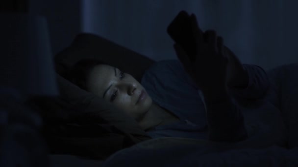 Woman lying in bed late at night and chatting with her smartphone, tech addiction and social media concept - Metraje, vídeo