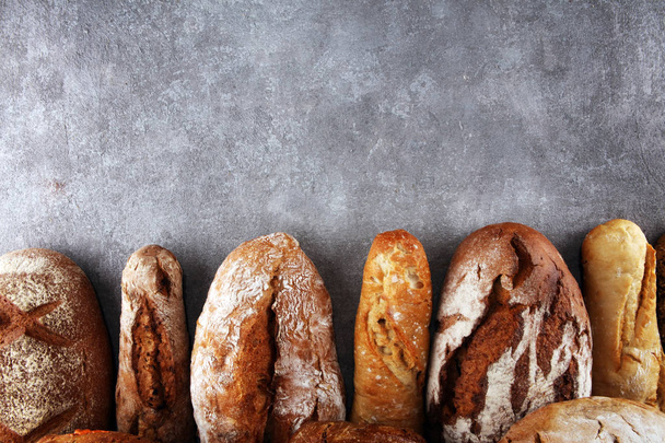 Surtido de panes horneados y panecillos sobre fondo de mesa de piedra. Concepto de cartel de panadería
 - Foto, Imagen