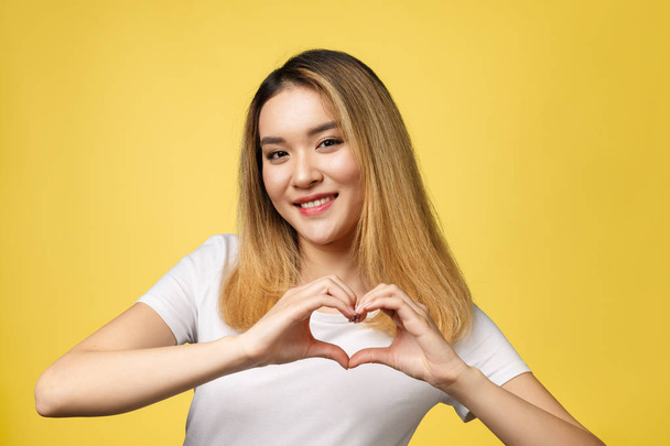 Jeune femme asiatique montrer signe de la main coeur isolé sur fond jaune
. - Photo, image