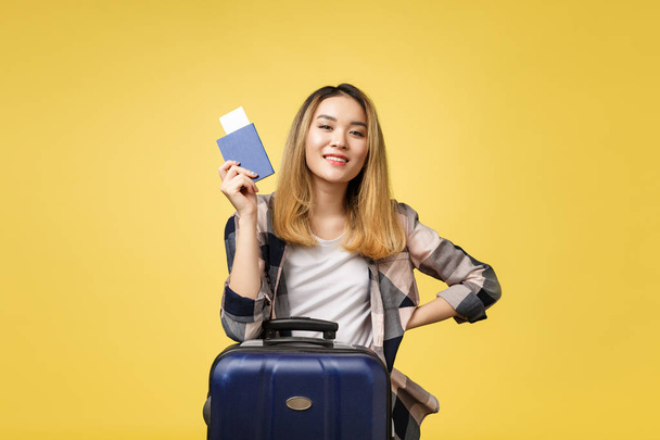 Женщина путешествует. Молодая красивая азиатка путешественница с паспортом, чемоданом и авиабилетом стоит над желтым
. - Фото, изображение