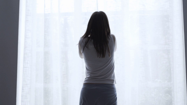 Heureuse femme détendue se réveillant et se levant du lit, elle ouvre les rideaux à la fenêtre
 - Séquence, vidéo