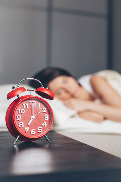Primer plano del reloj despertador y joven mujer dormida en el dormitorio en casa
 - Foto, Imagen