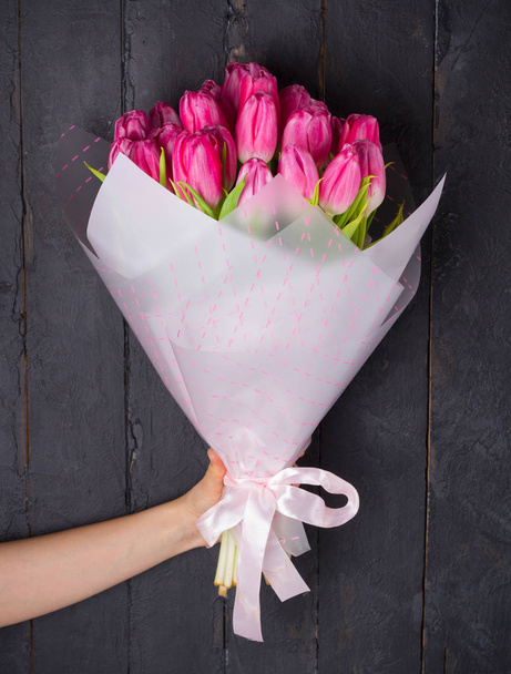 Woman hand holding bouquet of tulips flowers in packing on dark wood background - Φωτογραφία, εικόνα