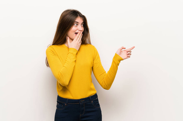 Young woman with yellow sweater pointing finger to the side with a surprised face - Foto, immagini