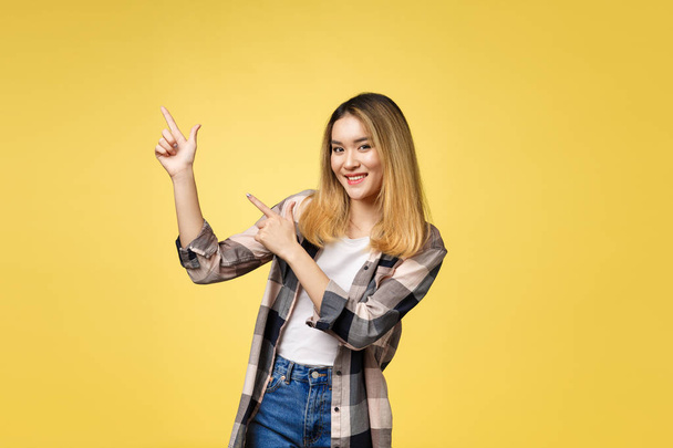 Smiling woman pointing finger side. Isolated portrait on yellow. - Photo, Image