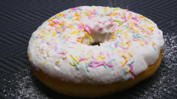 Close-up beregening gepoederde suiker donut gegarneerd met een glazuur in slow motion - Video