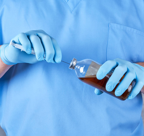 doctor in blue uniform holds a syringe and a glass bottle with injection, close up - Foto, Imagem