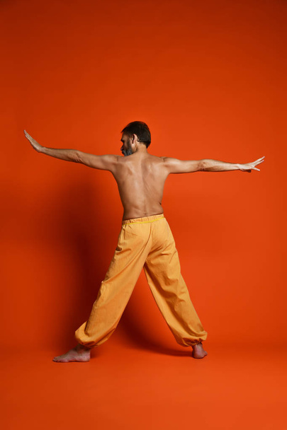 Old man practicing yoga doing stretching exercises against orange background - Fotó, kép