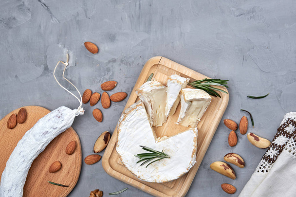 rundes Stück Brie-Käse und Wurst auf Holzbrett, grauer Hintergrund, Draufsicht, Kopierraum - Foto, Bild