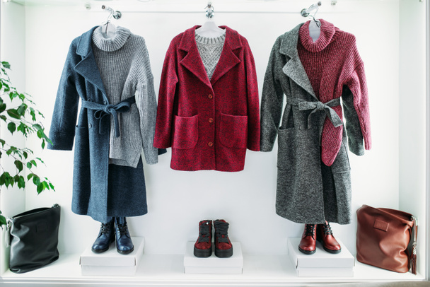 Showcase with female clothes in clothing store, nobody. Coats, jackets and shoes in fashion boutique - Photo, Image