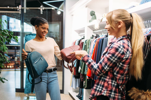 Twee vrouwtjes kiezen zakken in de winkel, winkelen. Shopaholics in kledingwinkel, consumentisme lifestyle, fashion - Foto, afbeelding