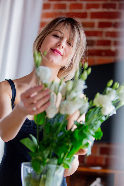 girl in a black dress is holding white roses before putting them in a vase - Фото, изображение
