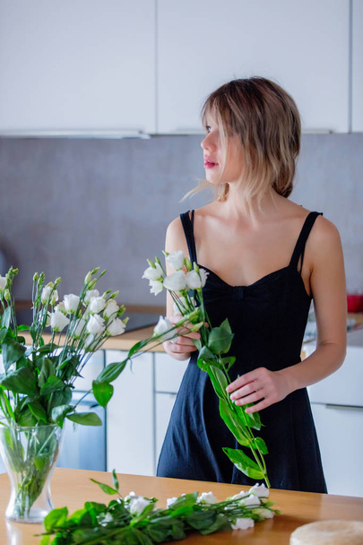 meisje in een zwarte jurk houdt witte rozen alvorens ze in een vaas - Foto, afbeelding