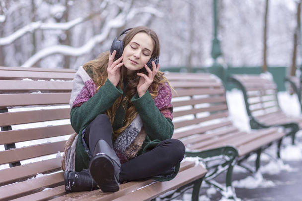 portrait of a woman enjoying music in headphones on a bench in winter - Fotoğraf, Görsel
