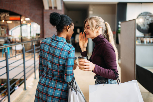 twee jonge aantrekkelijke vrouwen met boodschappentassen in winkelcentrum. Shopaholics in kledingwinkel, inkoop, vrouwelijke kopers in winkel - Foto, afbeelding