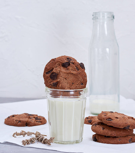 full glass of milk and round chocolate chip cookies, an empty milk bottle behind - Foto, Imagem