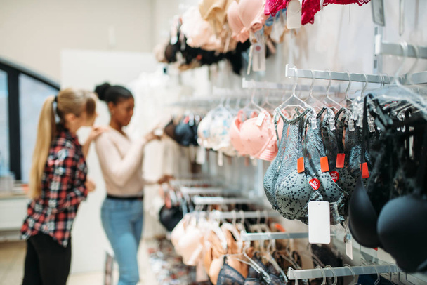 Kaksi naista valitsee alusvaatteet, shoppailee. Ostoskeskukset vaatekaupassa, kulutustottumukset, muoti, naisostajat alusvaateosastolla
 - Valokuva, kuva