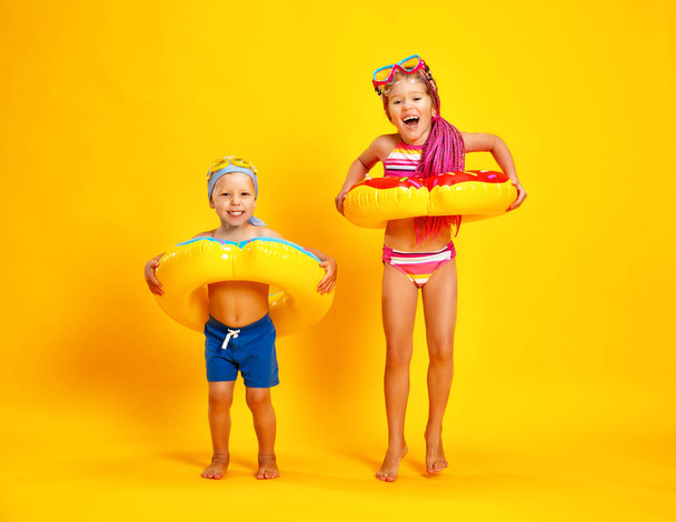 szczęśliwe dzieci dziewczynka i chłopiec w strój kąpielowy z pływania pierścień pączek na kolorowym tle żółty - Zdjęcie, obraz