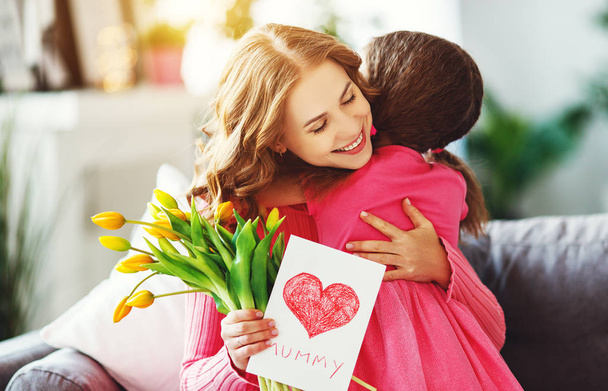 Gelukkige moederdag! kind dochter feliciteert moeder en geeft een boeket bloemen aan tulpen en postcar - Foto, afbeelding
