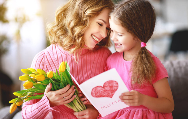 happy mother's day! child daughter congratulates mother and gives a bouquet of flowers to tulips and postcar - Zdjęcie, obraz