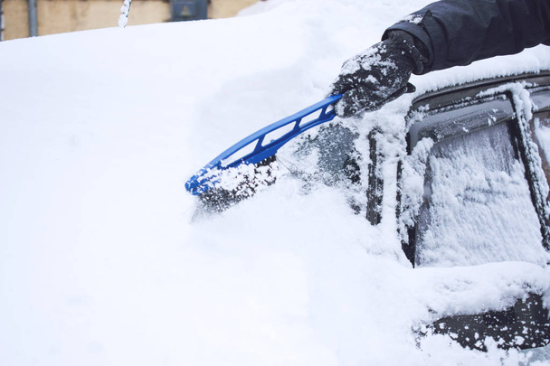 Człowiek czyszczenia samochodu ze śniegu i lodu z narzędziem pędzel i zgarniacz podczas opadów śniegu. Zimowe awaryjne. Wypadki związane z pogodą pojazdu. Samochodowe, pokryte śniegiem - Zdjęcie, obraz