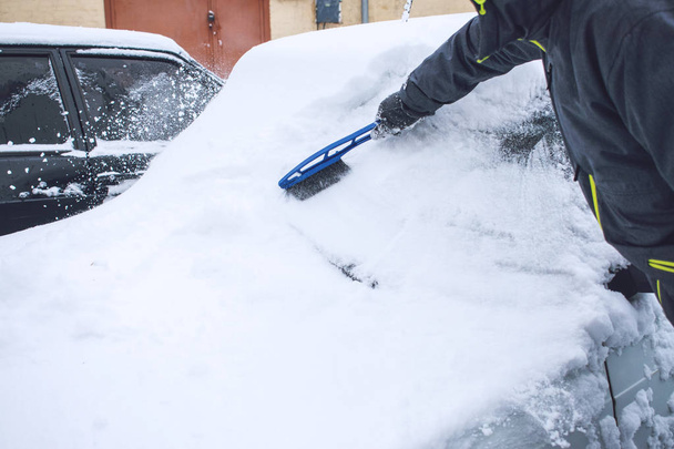 Muž čištění auta od sněhu a ledu s nástrojem štětec a škrabkou během sněžení. Zimní nouzové. Naléhavé případy související s počasím vozidla. Automobil sněhem - Fotografie, Obrázek