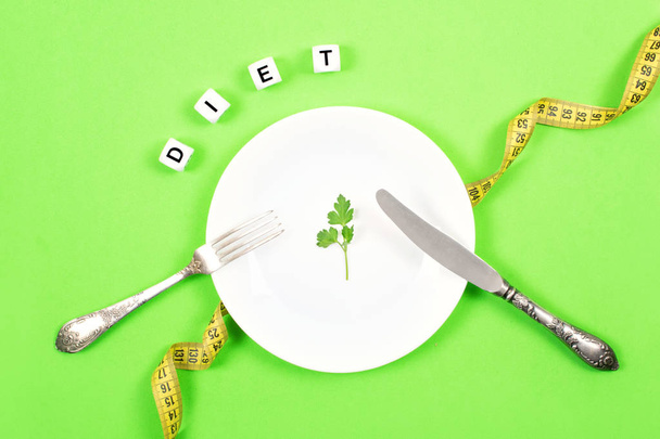ダイエット、損失、健康的な食事、フィットネスの概念の重量を量る。大きな板の上に食べ物の小さな部分。測定テープのバック グラウンドにフォークとナイフとテキストの食事と白いプレートに小さなグリーン サラダ葉. - 写真・画像