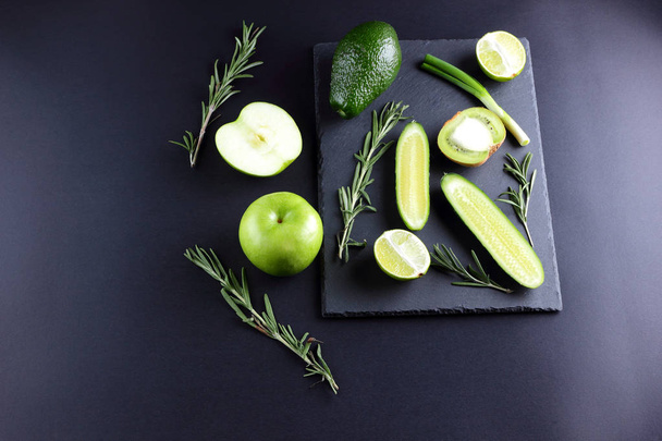 Green fruits and vegetables on dark slate board. Concept of natural green products. Avocado, kiwi, lime and apple on dark background. Rosemary, dill and chives on stone board - Photo, Image