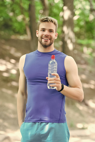 Athlete drinks water after training in park on sunny day. Man athletic attractive appearance holds water bottle. Man athlete sport clothes training outdoor. Sport and healthy lifestyle concept - Foto, Bild