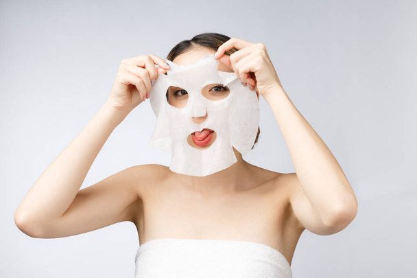 hermosa asiático mujer aplicación papel hoja máscara en su cara blanco fondo - Foto, imagen