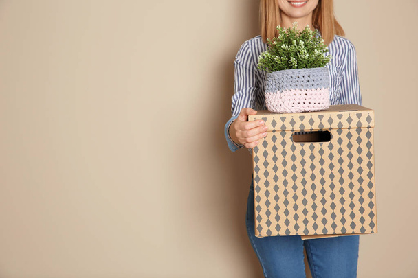 Woman with moving box and plant on color background. Space for text - Fotografie, Obrázek