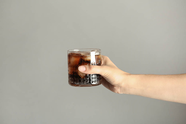 Woman holding glass of tasty refreshing cola with ice cubes on color background, closeup view - 写真・画像
