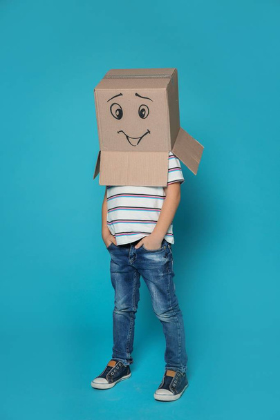Cute little child wearing cardboard box with smiling face on color background - Fotó, kép