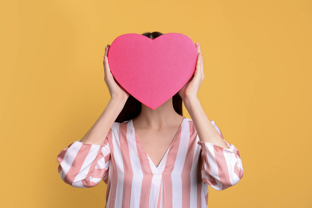 Young woman with decorative heart near face on color background - 写真・画像