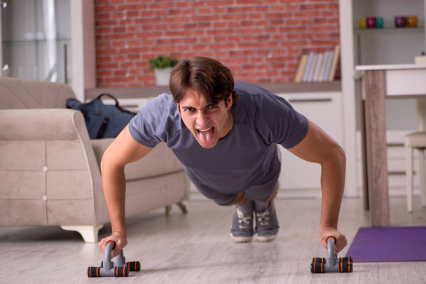 Όμορφος νεαρός κάνει αθλητισμό ασκήσεις στο σπίτι  - Φωτογραφία, εικόνα