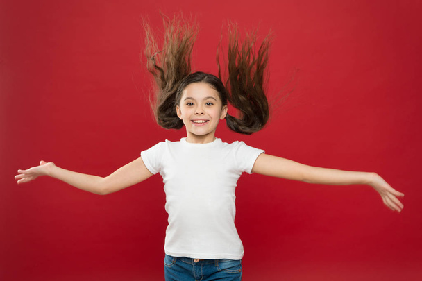 Kid smiling cute face live carefree happy life. Enjoy every moment. Young and free. Happy child girl with long hair on red background. Happiness and joy. Positive emotions. Child care and upbringing - Fotó, kép