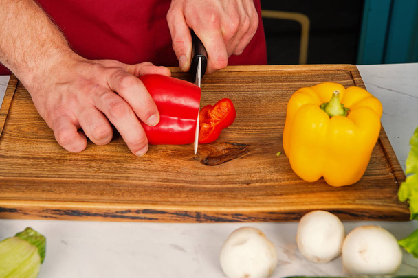 Hand slice pepper with ceramic knife. Vegetables getting cut on wooden cutting board. Food preparation and cooking recipes. Vegetarian menu and healthy diet. Organic products concept - Φωτογραφία, εικόνα