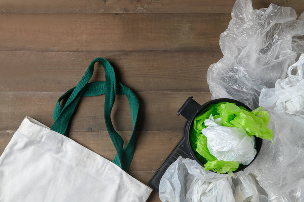 bolsas de plástico en contenedor y bolsa de lona sobre fondo de madera, rechazar el plástico o reciclar y ahorrar concepto ambiental
 - Foto, Imagen