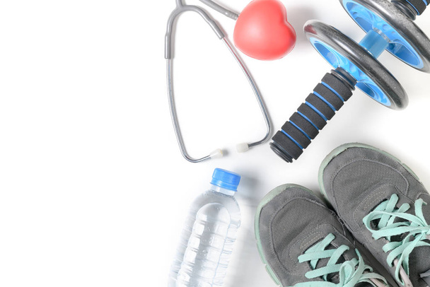 Sapatilhas e roda de fitness com estetoscópio isolado em fundo branco, dieta e exercício para perder o conceito de peso
 - Foto, Imagem