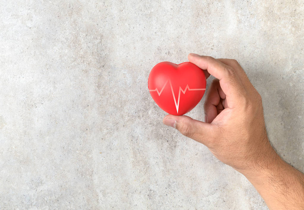 Ο άνθρωπος που κρατώντας μια κόκκινη καρδιά σχήμα στο μαρμάρινο τραπέζι. υγειονομικής περίθαλψης αγάπη, δίνουν, ελπίδα και παγκόσμια ημέρα καρδιάς - Φωτογραφία, εικόνα