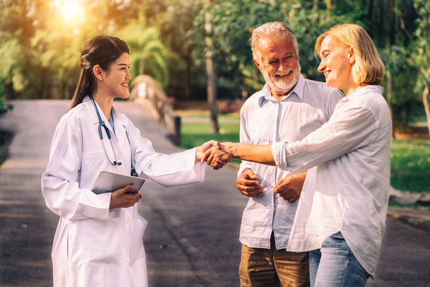 Senior couple man and woman talking to young nurse or caregiver in the park. Mature people healthcare and medical staff service concept. - Photo, Image