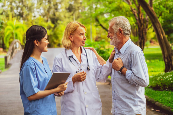 Senior man talking to doctor, nurse or caregiver in the park. Mature people healthcare and medical staff service concept. - Photo, Image