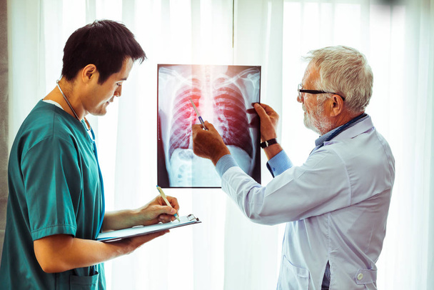Ein leitender Arzt betrachtet den Röntgenfilm einer Brustverletzung des Patienten, während er mit einem anderen Arzt im Krankenhaus zusammenarbeitet. medizinisches Gesundheitspersonal und ärztlicher Dienst. - Foto, Bild