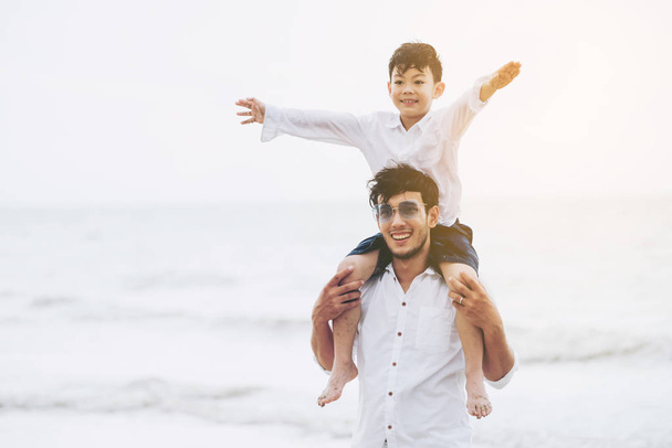 Pai feliz carregando seu filho no pescoço em uma praia de areia tropical no verão
. - Foto, Imagem