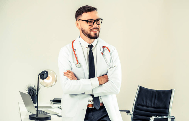 Male doctor crossed arms standing at office table in the hospital. Medical and healthcare concept. - Photo, Image