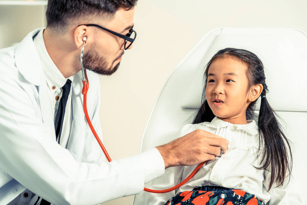 Νεαρά αρσενικά γιατρός εξετάζει παιδάκι στο νοσοκομείο γραφείο. Το παιδί είναι ευτυχισμένο και δεν φοβάται ο γιατρός. Ιατρική παιδιά υγειονομικής περίθαλψης έννοια. - Φωτογραφία, εικόνα